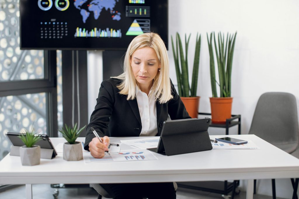 Beautiful purposeful middle aged blond Caucasian businesswoman in formal clothes, working with