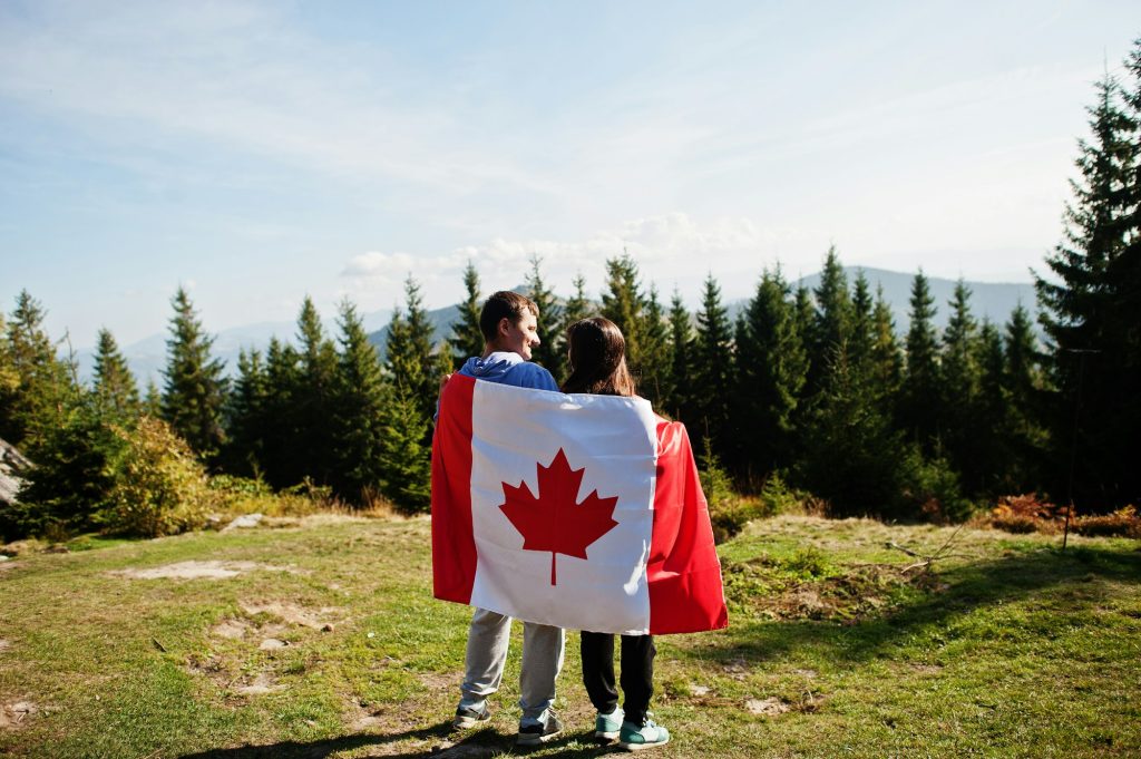 Happy Canada Day. Couple with large Canadian flag celebration in mountains.